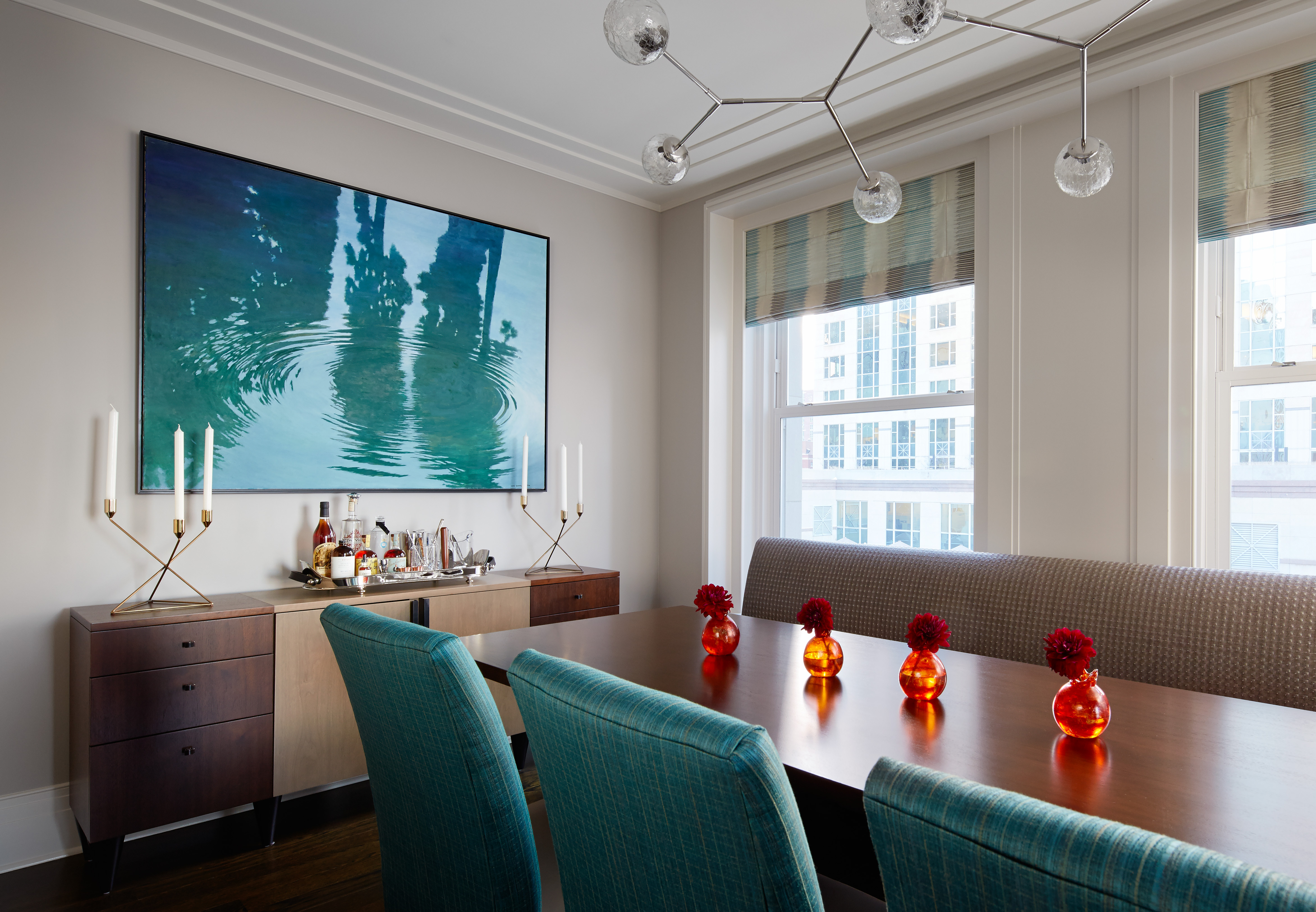 Bright and Vibrant Dining Room incorporates blue water ripple artwork, vibrant blue chairs, wooden sideboard, with abstract chandelier