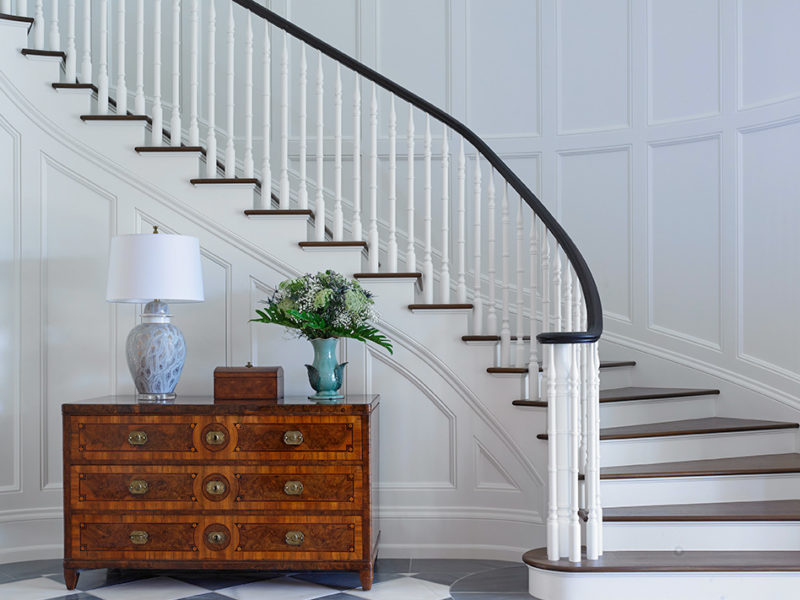Bright and coastal foyer design incorporates Antique Chest of Drawers by Olivier Fluery, placed beautifully amongst spiral staircase.