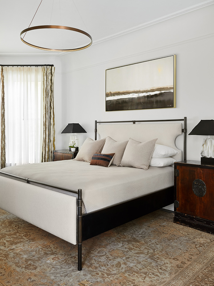 Bedroom incorporates antique rug, upholstered bed, halo chandelier, and landscape art.