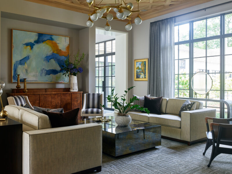 Beautiful living room design incorporating wooden media cabinet, glass and brass chandelier, mirrored coffee table, and upholstered sofas.