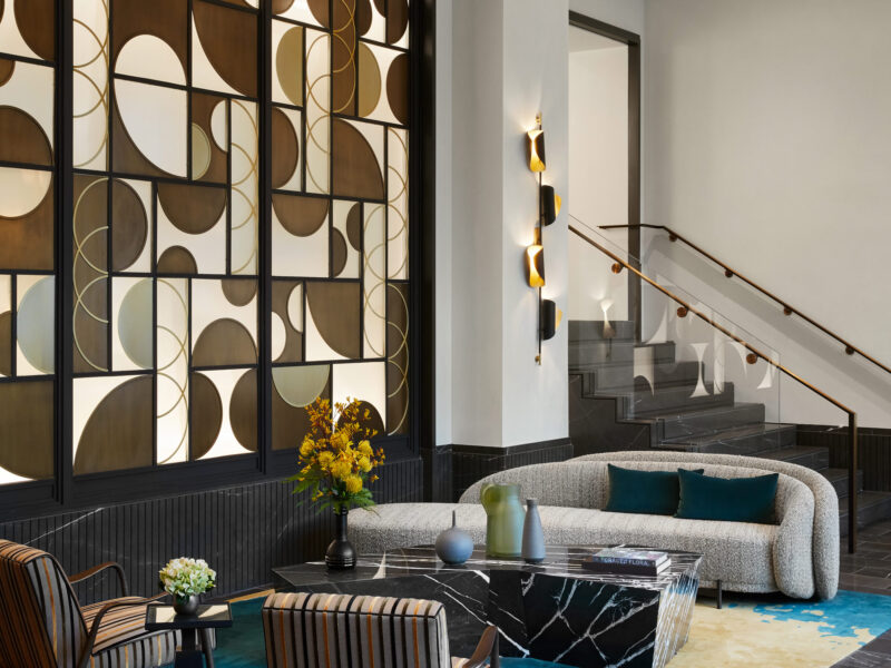 Apartment Waiting Area incorporating Black Marble Coffee Table, Striped Holly Hunt Lounge Chairs, Blue and Gold SHIIR Rug, and Glass Wall Paneling