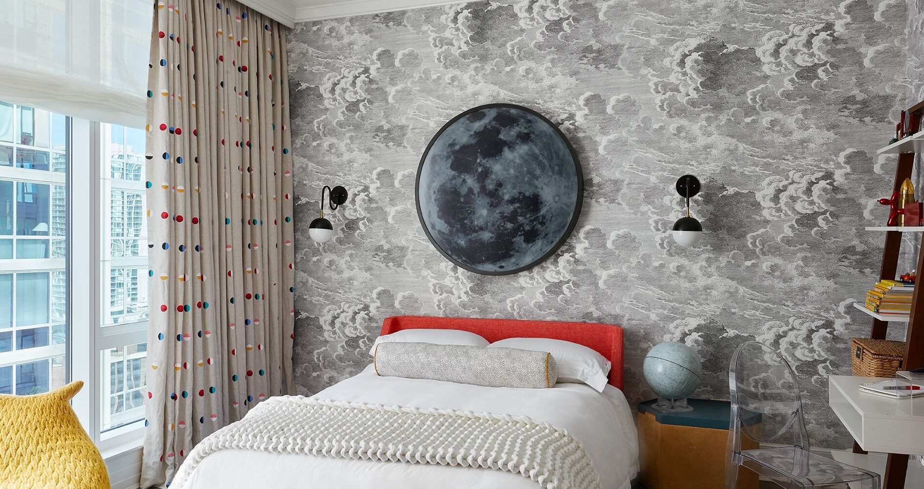 Boys Bedroom incorporating grey clouds wallcovering, red upholstered bed, moon light above bed.